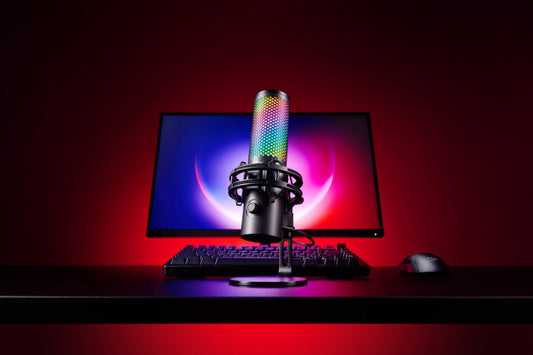 HyperX RGB microphone on a desk in a modern streaming setup with a glowing monitor in the background.