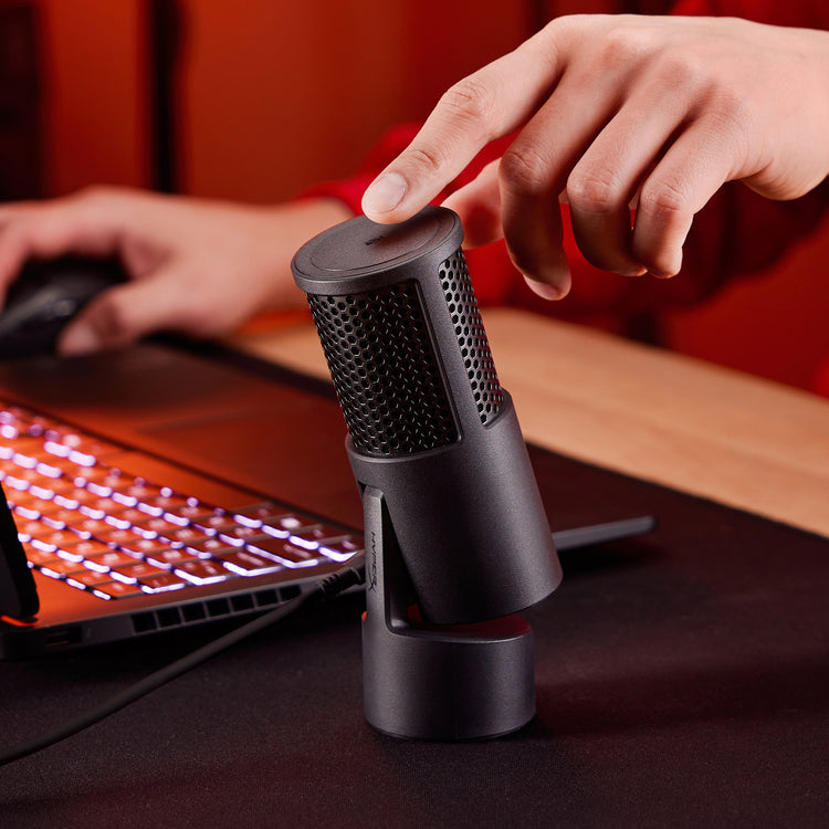 Person using a black SoloCast 2 microphone on a desk with a laptop in the background